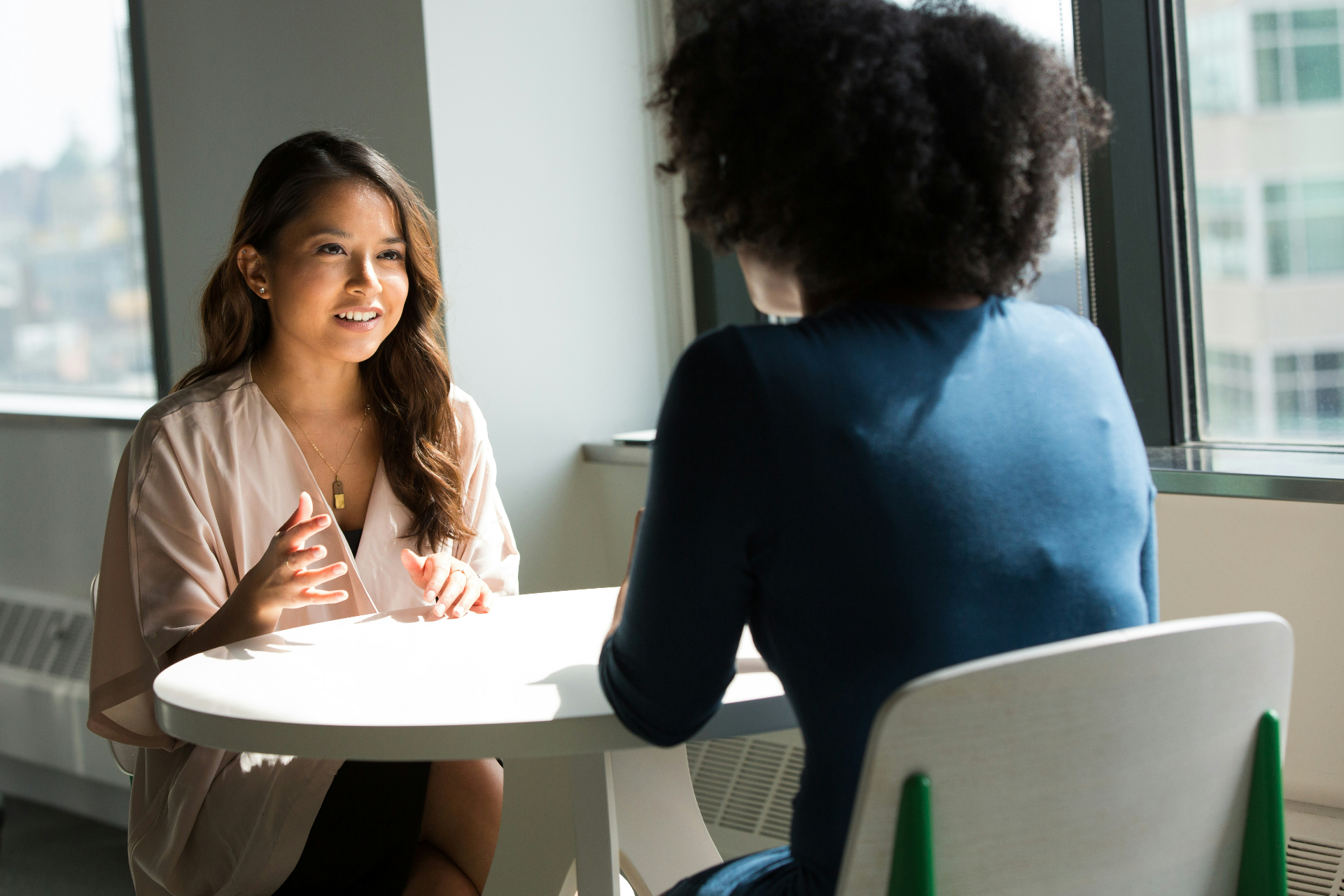 Two women in a focused one-to-one conversation by a bright window